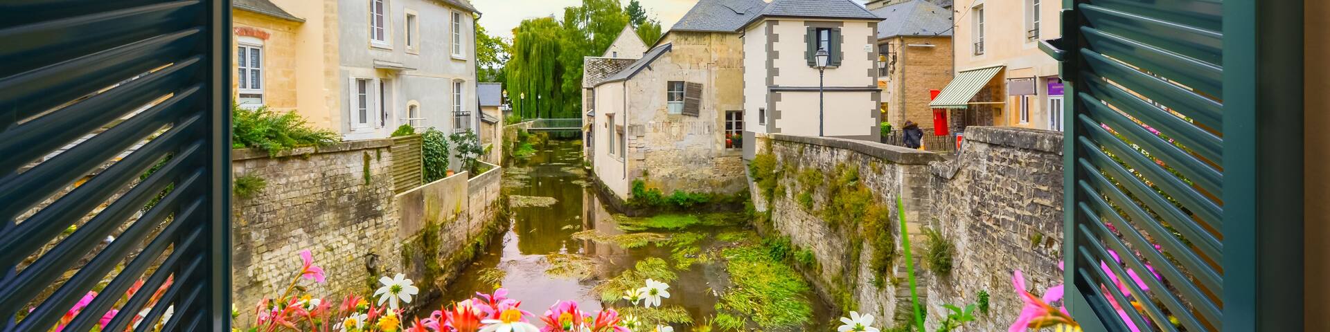 A narrow waterway flanked by historic buildings, with a vibrant flower display in the foreground.