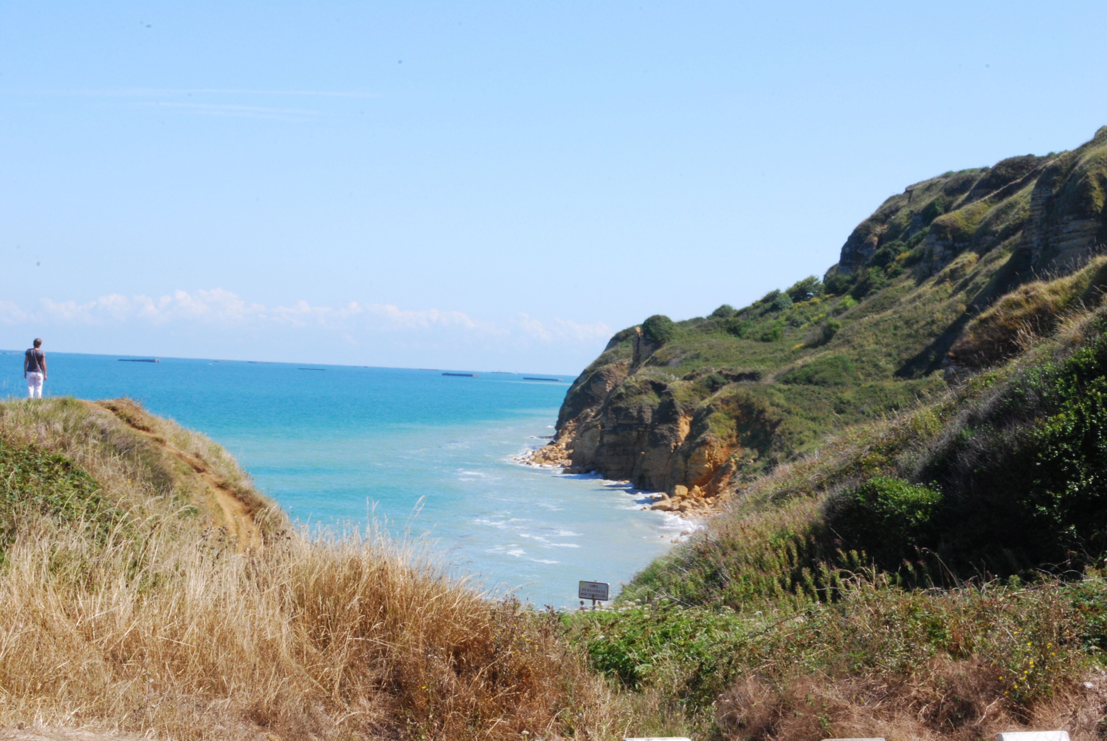 A coastal landscape with a person standing on a cliff overlooking the sea.