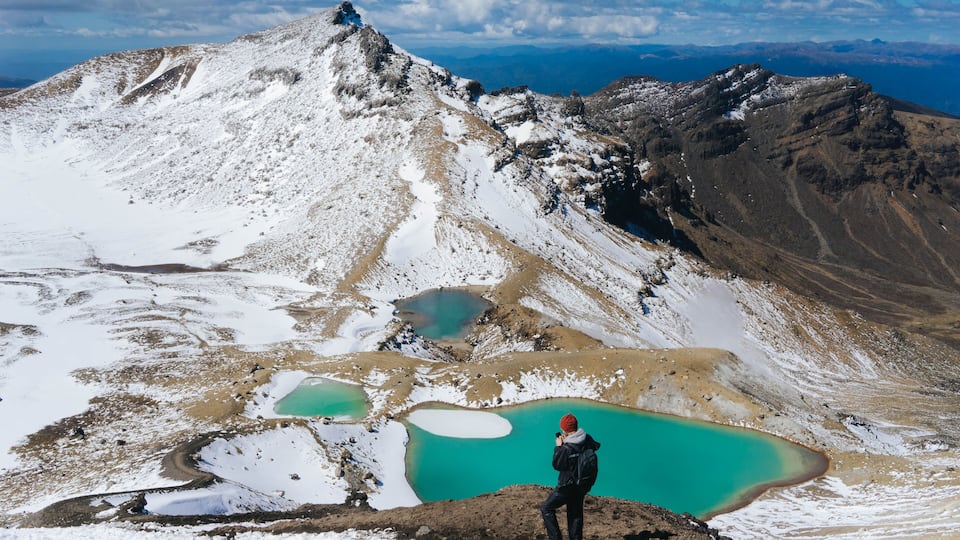 A hiker taking a photo of a mountain range with a turquoise lake at its base.