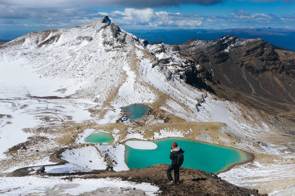 A hiker taking a photo of a mountain range with a turquoise lake at its base.