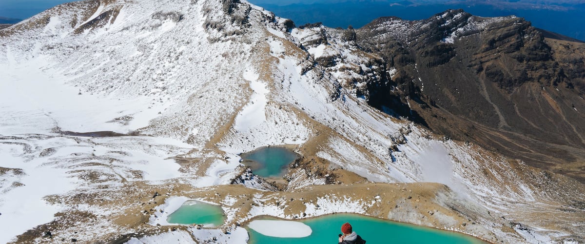 A hiker taking a photo of a mountain range with a turquoise lake at its base.