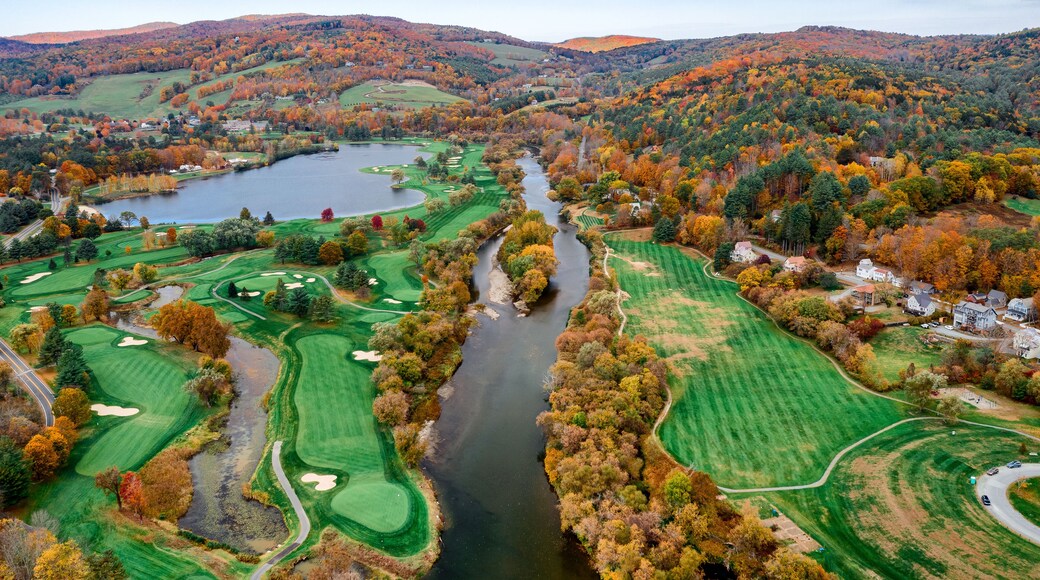 Aerial view of the Connecticut River snaking through a vibrant tapestry of fall foliage near a golf course and lake, White River Junction, Vermont, United States.