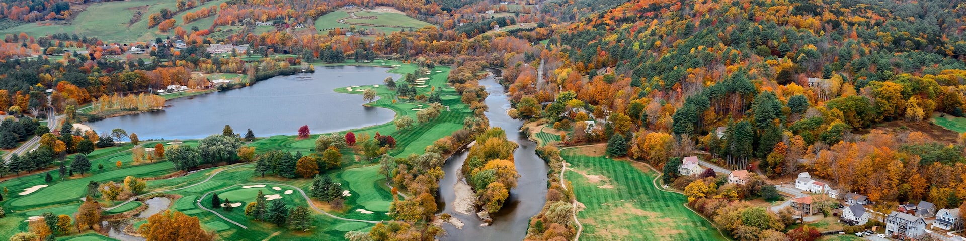 Aerial view of the Connecticut River snaking through a vibrant tapestry of fall foliage near a golf course and lake, White River Junction, Vermont, United States.