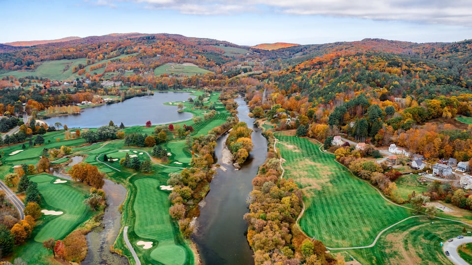 Aerial view of the Connecticut River snaking through a vibrant tapestry of fall foliage near a golf course and lake, White River Junction, Vermont, United States.