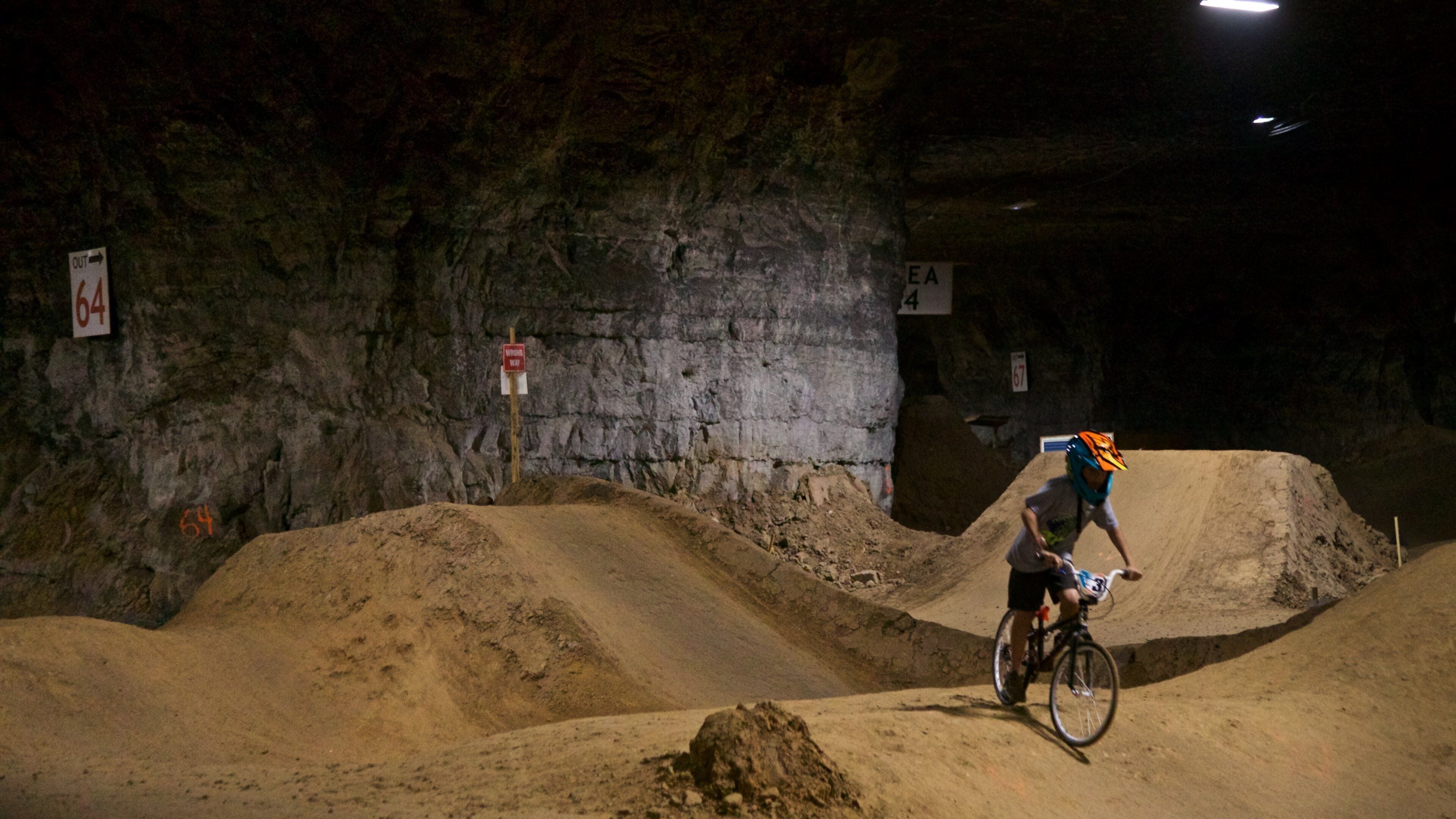 Un cycliste de BMX sur une piste de terre, avec un mur rocheux en arrière-plan.