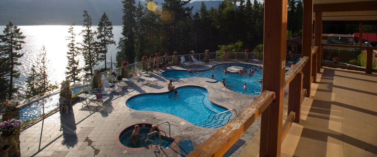 A pool area with multiple pools and a view of a lake and mountains.