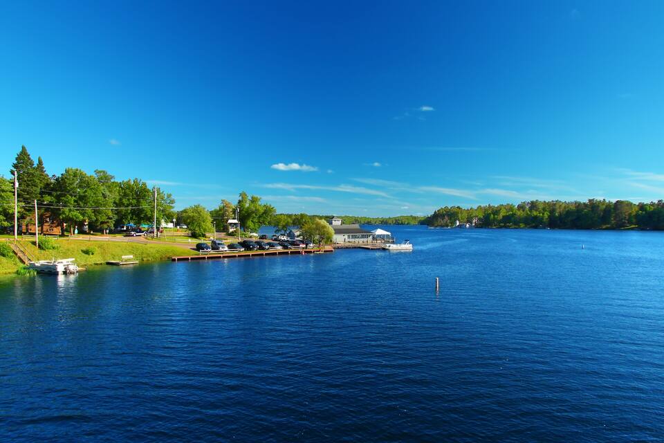 Un lago tranquilo con un muelle, barcos y un pequeño edificio.
