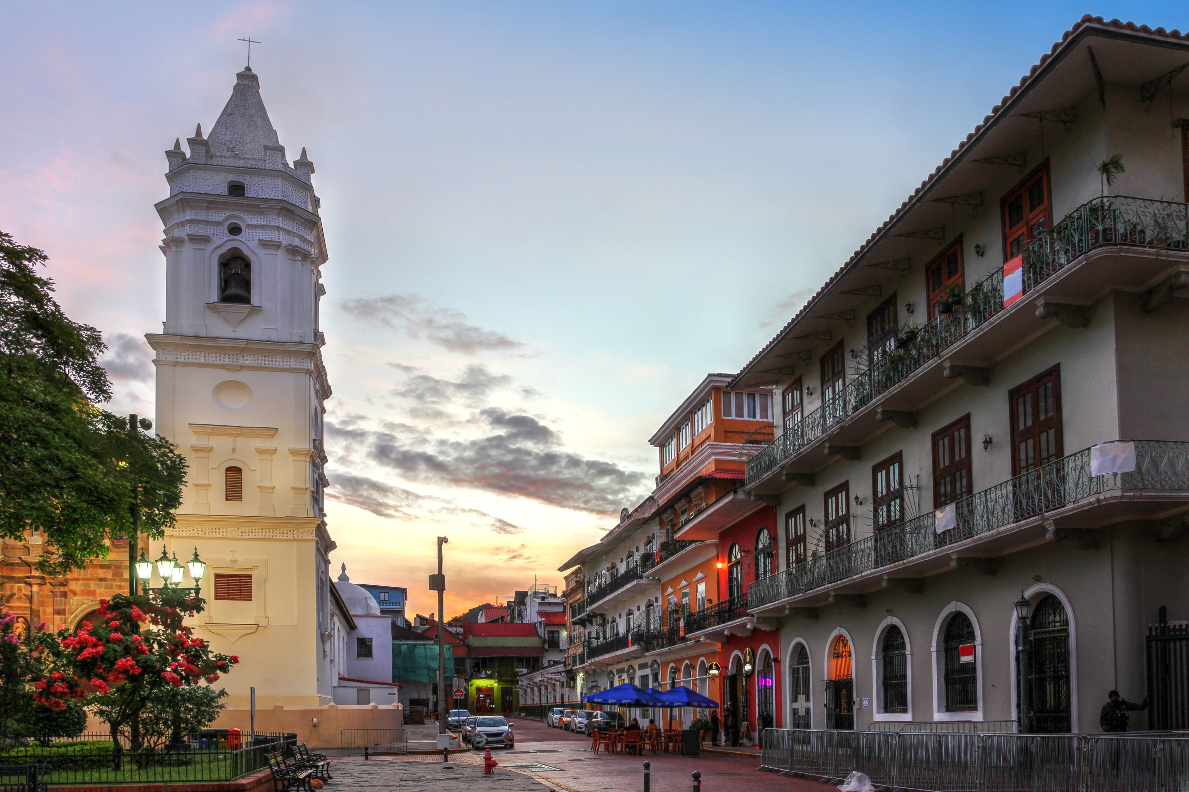 Una calle histórica con una torre de iglesia, edificios coloridos y un cielo al atardecer.
