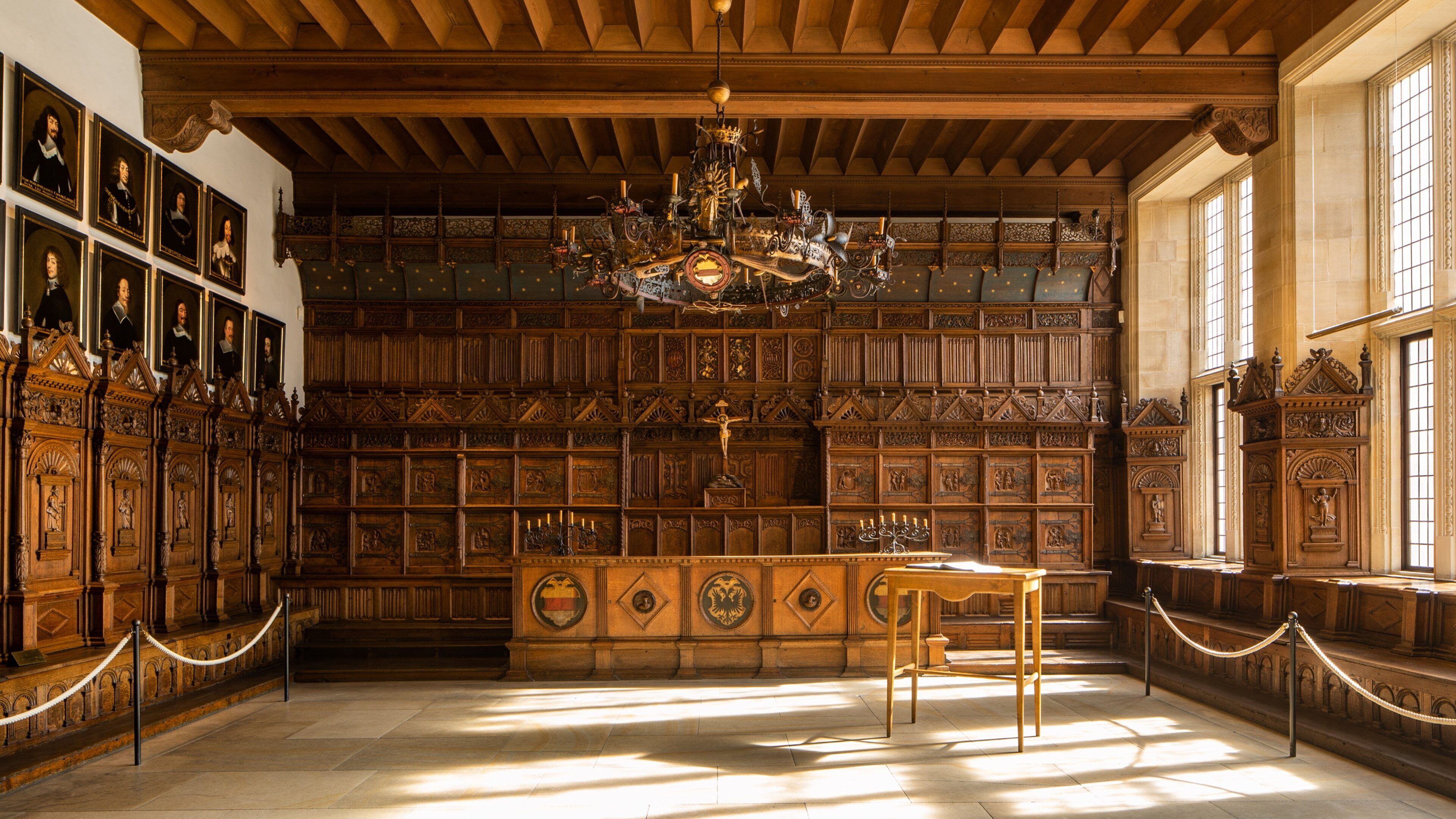 Um salão imponente com altar de madeira, um candelabro e retratos emoldurados nas paredes.