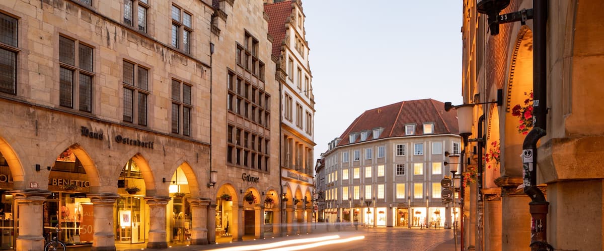 A cobblestone street lined with historic buildings, including a prominent archway and a building with a sign reading "BENETTO".