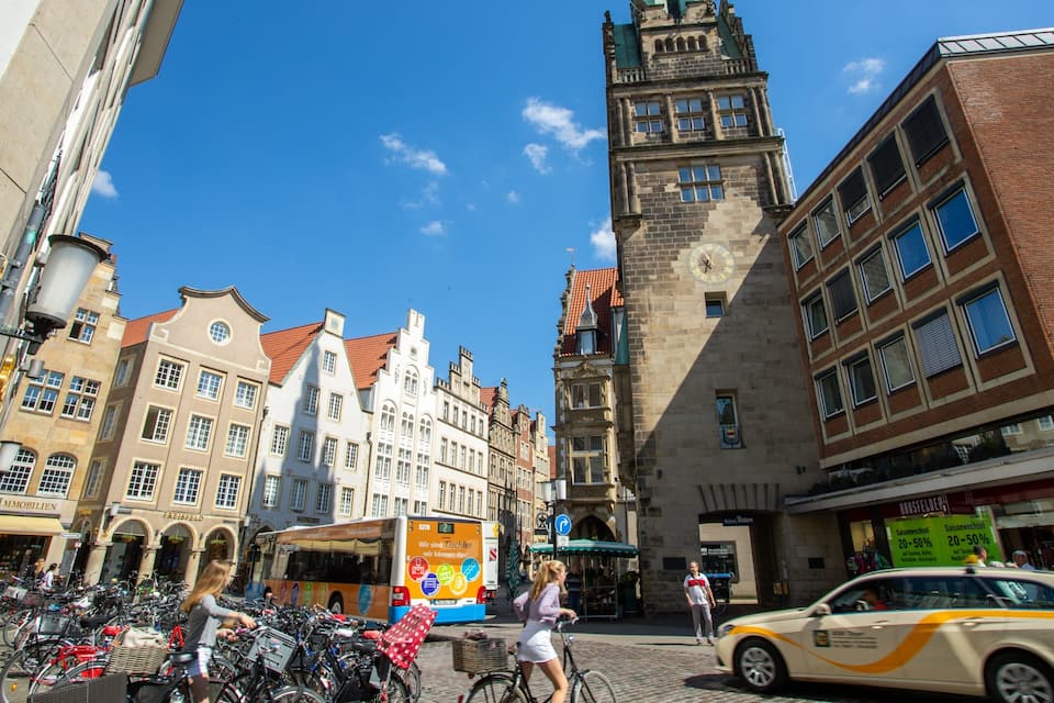A cobblestone street lined with historic buildings, a clock tower, and a tram.