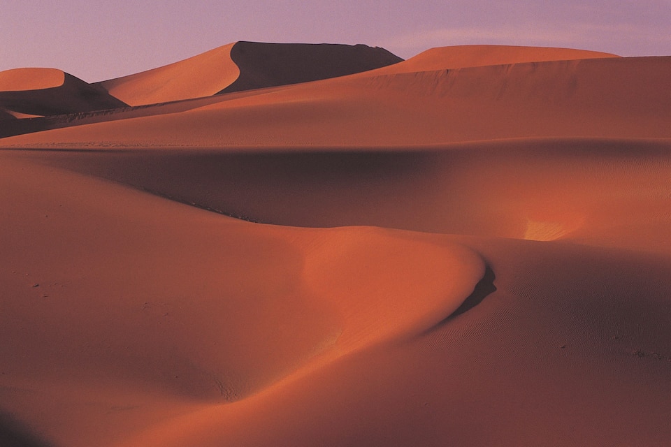 A desert landscape with rolling sand dunes under a clear sky.