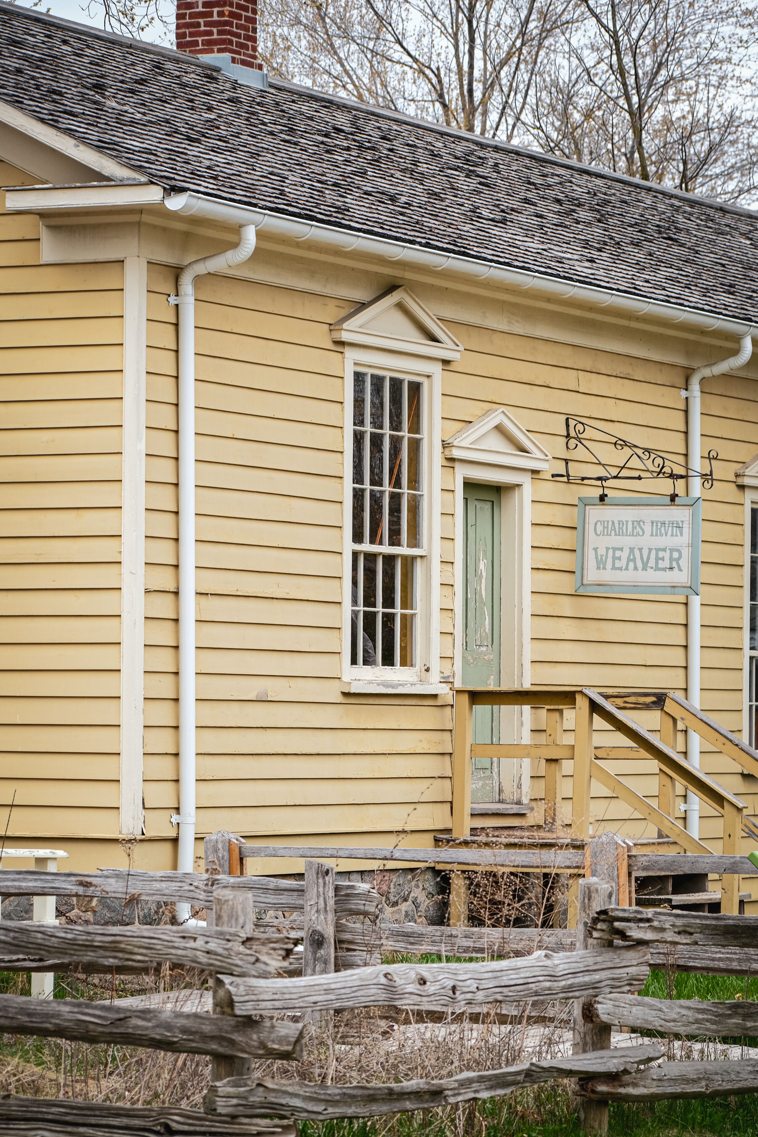 A yellow building with a sign reading 'Charles Irvin Weaver,' a wooden staircase, and a weathered fence.