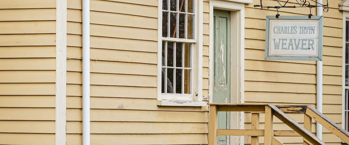 A yellow building with a sign reading 'Charles Irvin Weaver,' a wooden staircase, and a weathered fence.
