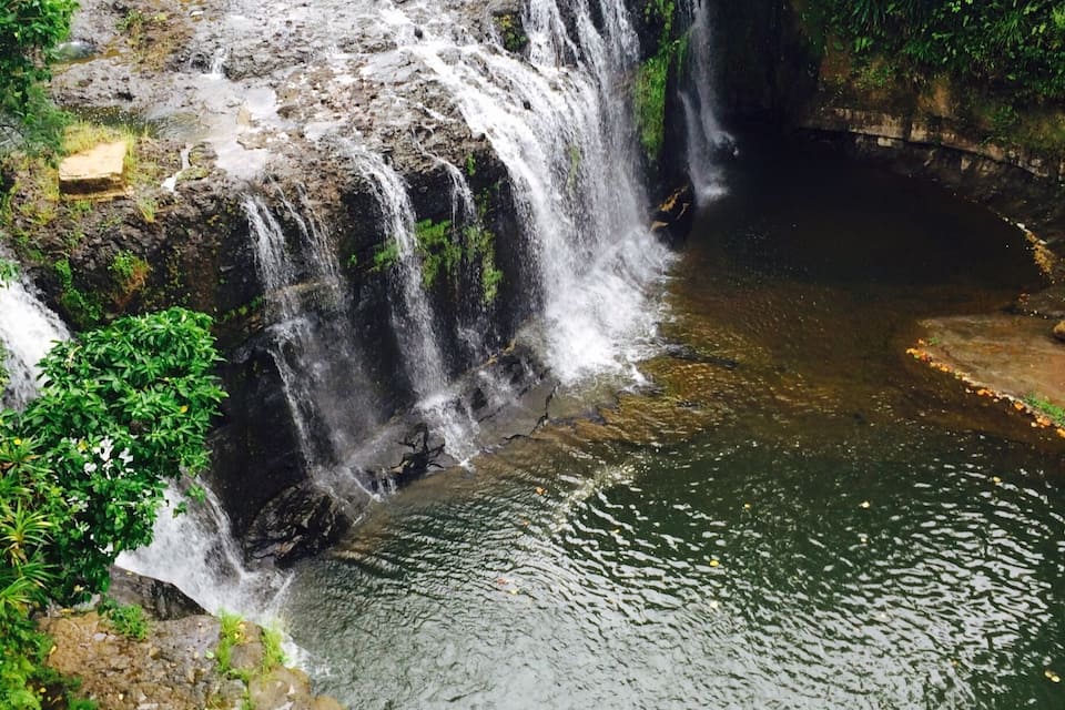 Una cascada que s'aboca sobre un penya-segat cap a un riu envoltat de vegetació exuberanta.