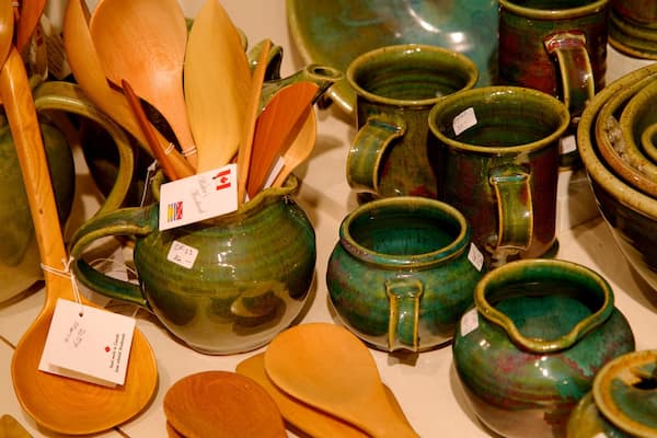 Une variété d’ustensiles de cuisine en céramique, notamment des cuillères en bois, des bols et des cruches, sont exposés sur une table.
