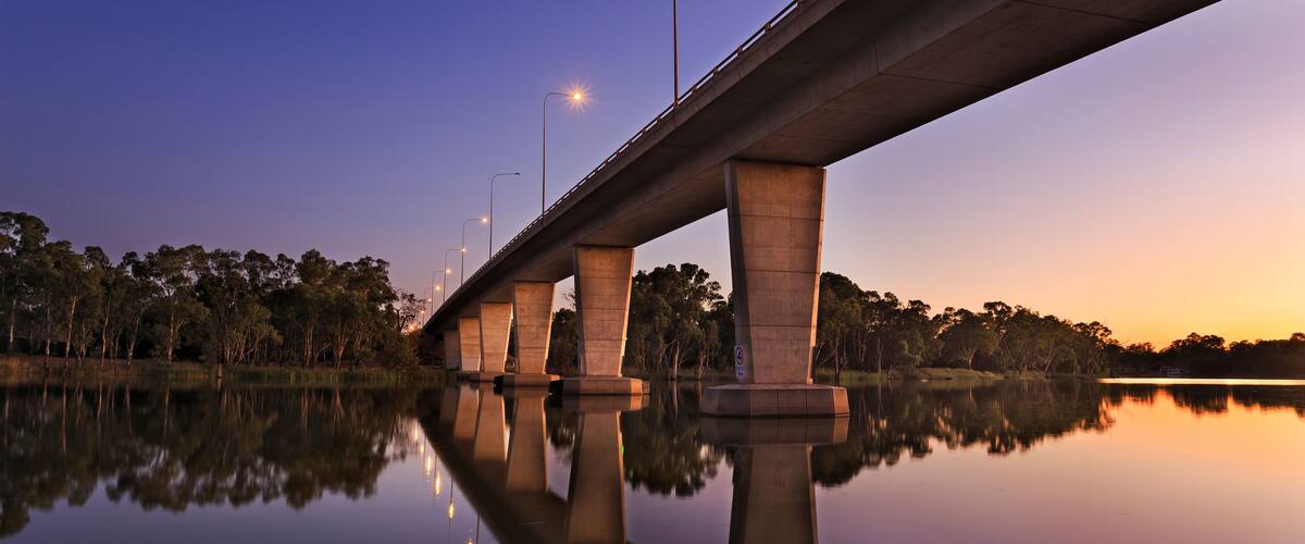 A bridge over calm water with trees on the banks and streetlights along the bridge.