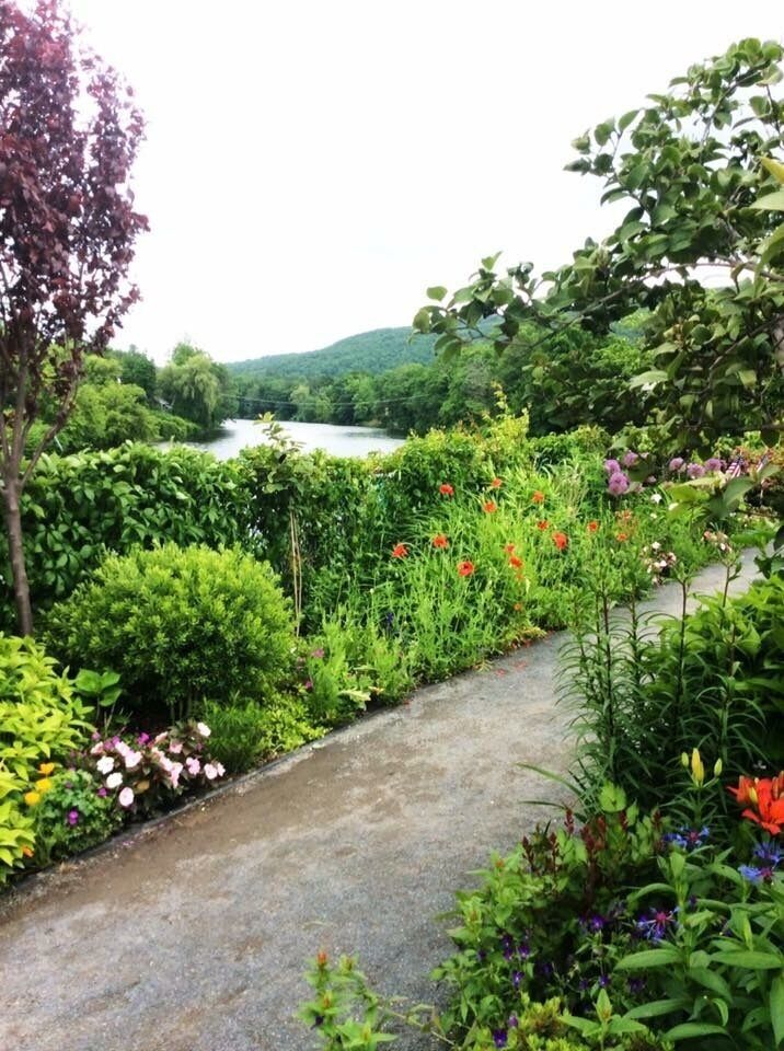 A garden with a pathway, various plants, and a river in the background.