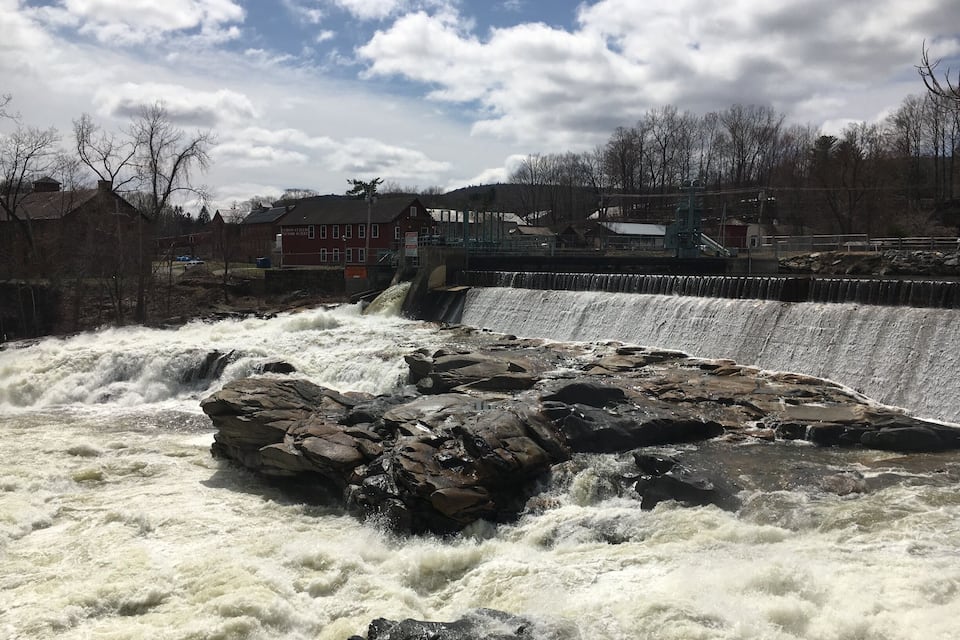 A dam with a waterfall and a town in the background.
