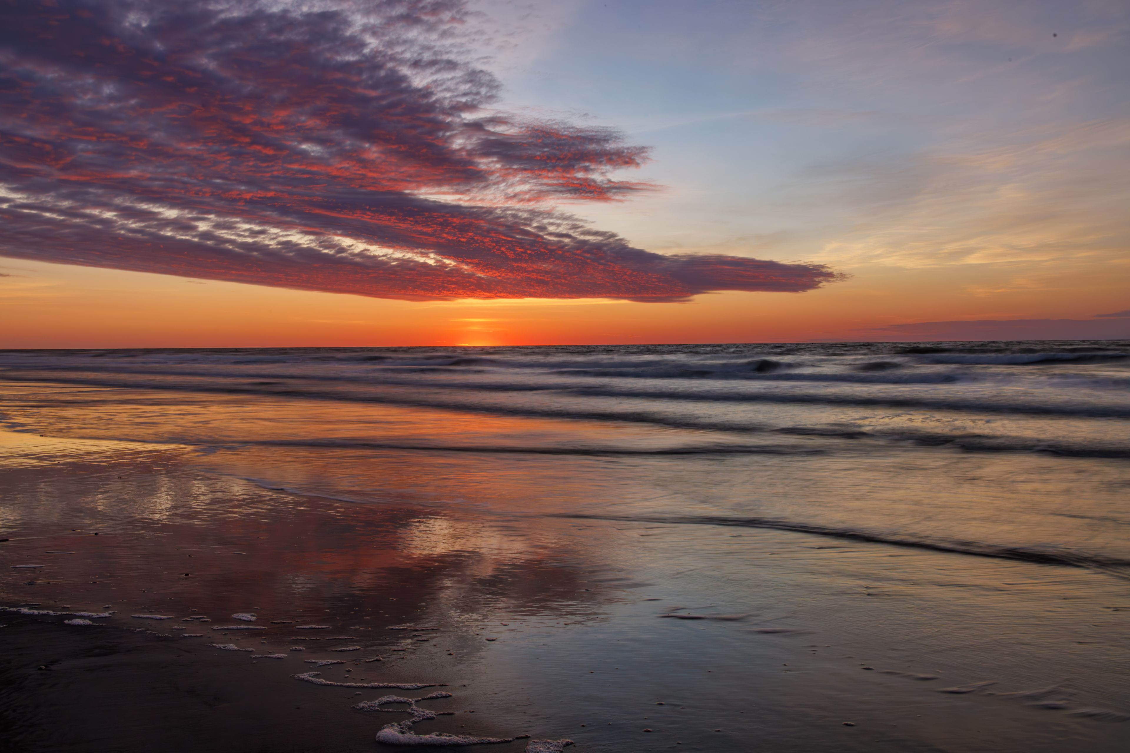 Colorful sunrise over the Atlantic Ocean with dramatic clouds reflecting on wet sand in Wildwood, New Jersey