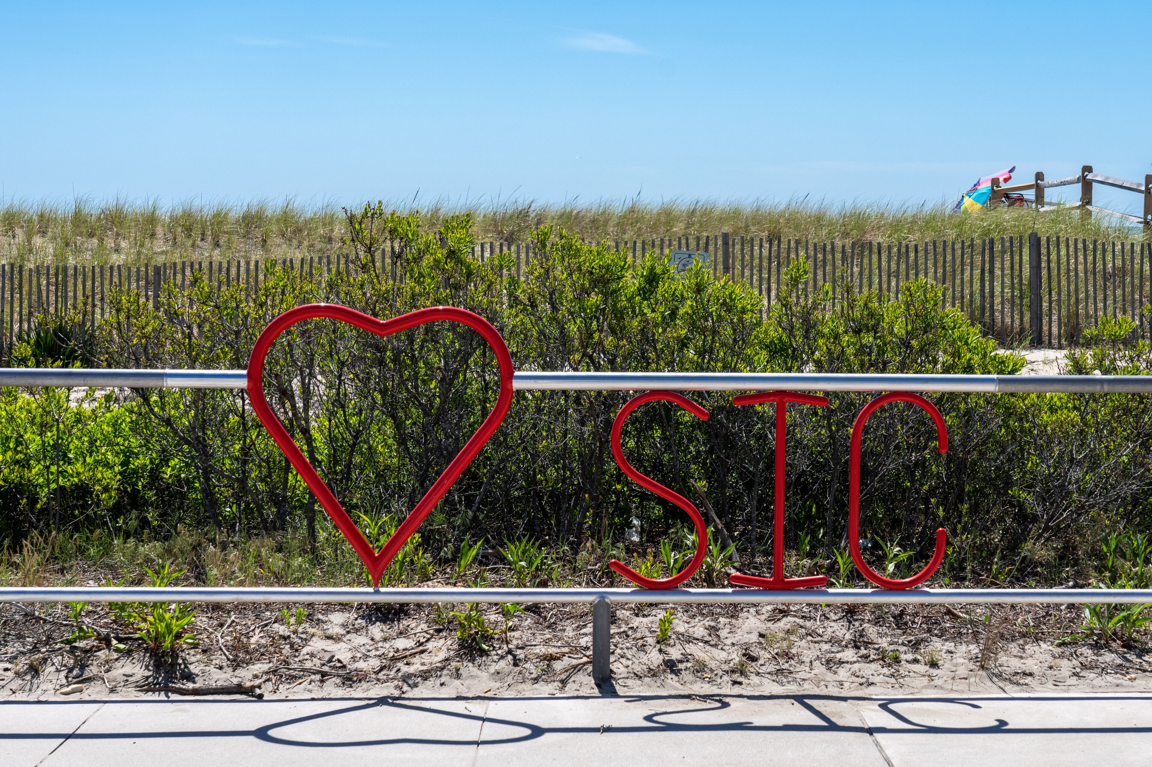 A beach with a fence, a heart-shaped sign, and the letters 'SIC' in red.