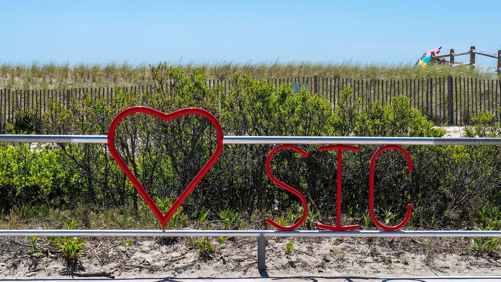 A beach with a fence, a heart-shaped sign, and the letters 'SIC' in red.