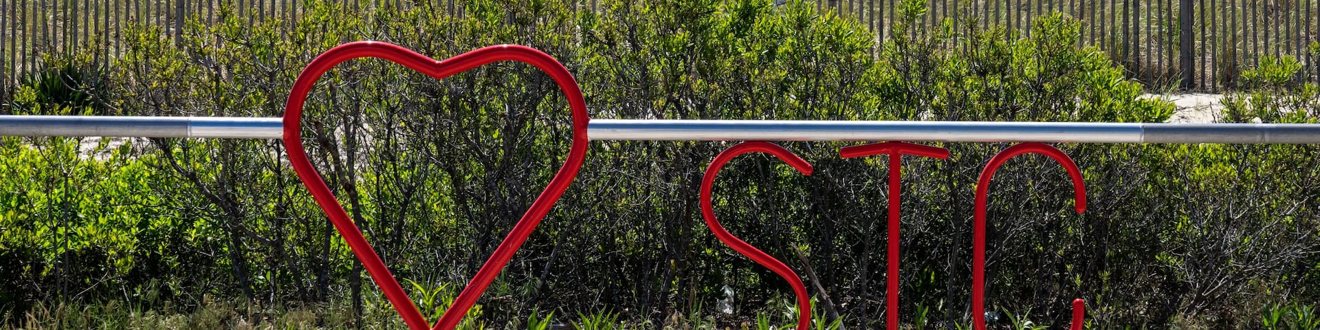 A beach with a fence, a heart-shaped sign, and the letters 'SIC' in red.