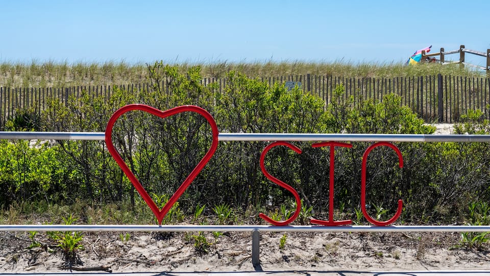 A beach with a fence, a heart-shaped sign, and the letters 'SIC' in red.