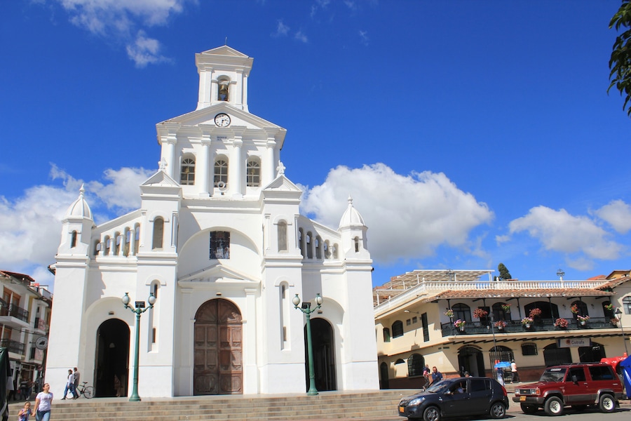 Une église blanche dotée d’un clocher et d’une horloge, entourée d’immeubles et de voitures.