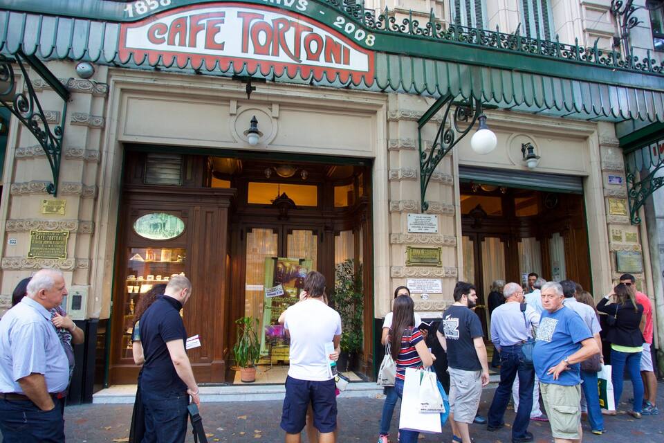 Un caffè chiamato Cafe Tortoni con tendaggi verdi decorati e un cartello d'epoca.