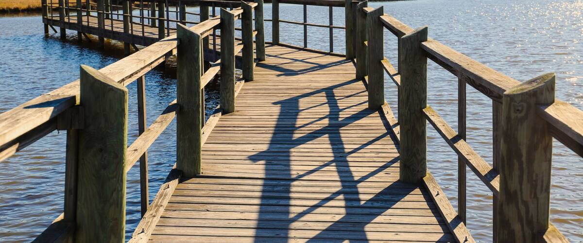 a long gray wooden bridge on the vast blue lake water of Lake McIntosh with stunning skies and lush green and autumn colored trees on the banks of the lake at Lake McIntosh in Peachtree City Georgia