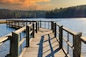 a long gray wooden bridge on the vast blue lake water of Lake McIntosh with stunning skies and lush green and autumn colored trees on the banks of the lake at Lake McIntosh in Peachtree City Georgia