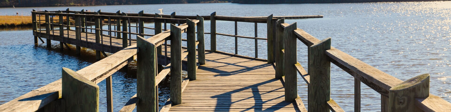 a long gray wooden bridge on the vast blue lake water of Lake McIntosh with stunning skies and lush green and autumn colored trees on the banks of the lake at Lake McIntosh in Peachtree City Georgia