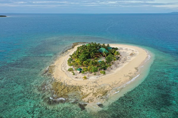 A tropical island with clear turquoise waters, a sandy beach, and lush greenery.