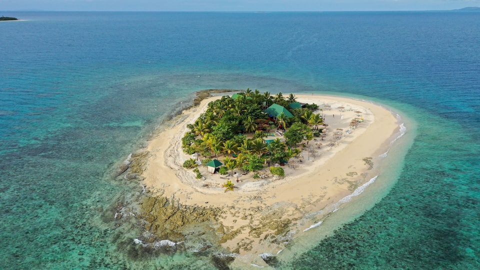 A tropical island with clear turquoise waters, a sandy beach, and lush greenery.