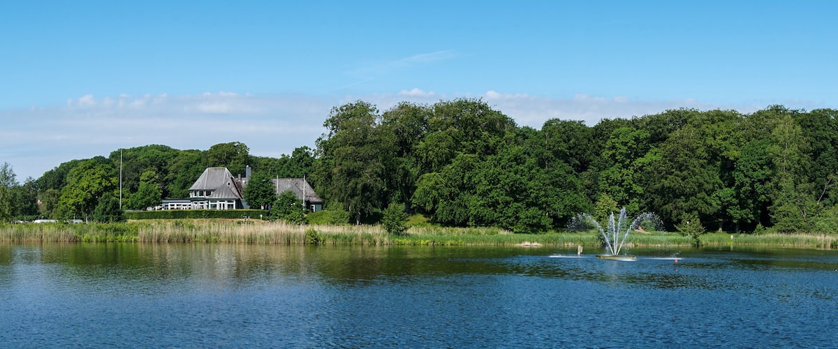 A lake with a house and dense forest in the background.