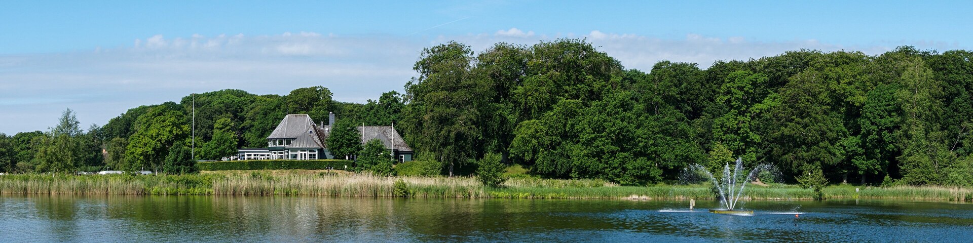A lake with a house and dense forest in the background.