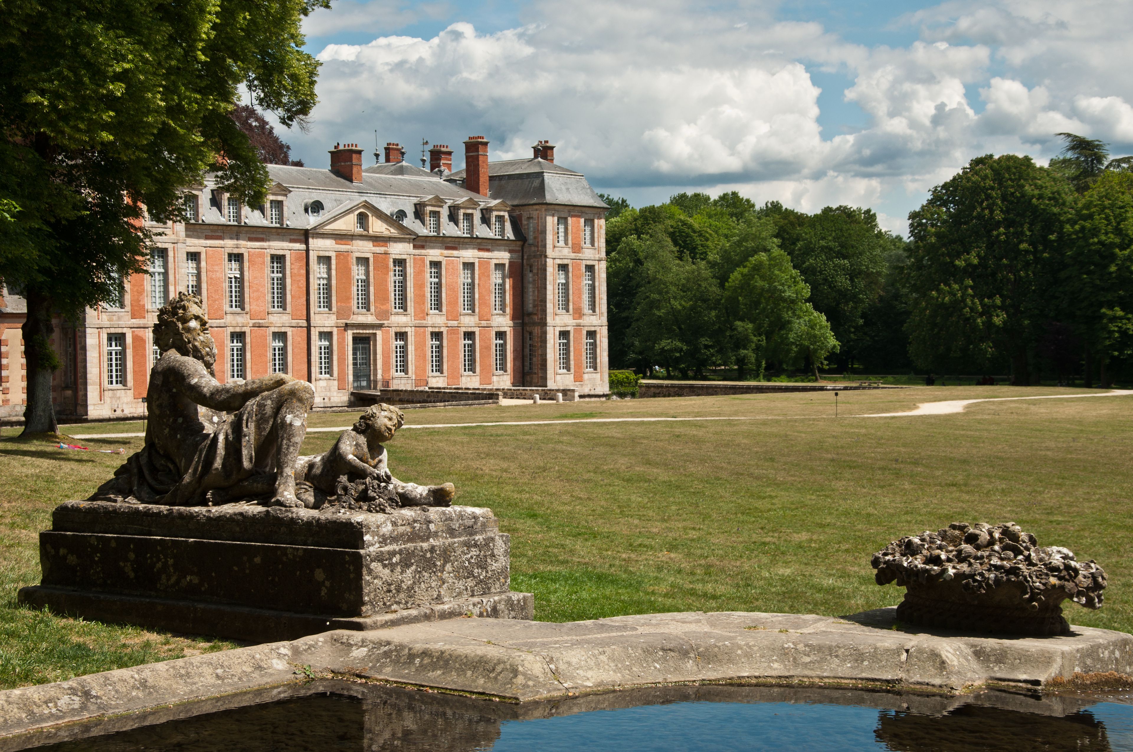 A classical statue in a garden with a large building in the background.