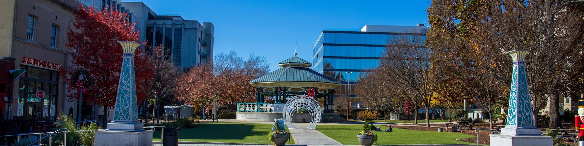 a gorgeous autumn landscape at the Decatur Square with red and yellow autumn trees, lush green trees and a round blue pergola, glass office buildings and clear blue sky in Decatur Georgia USA
