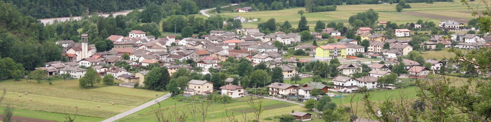A village nestled in a valley with houses, a church, and surrounding greenery.