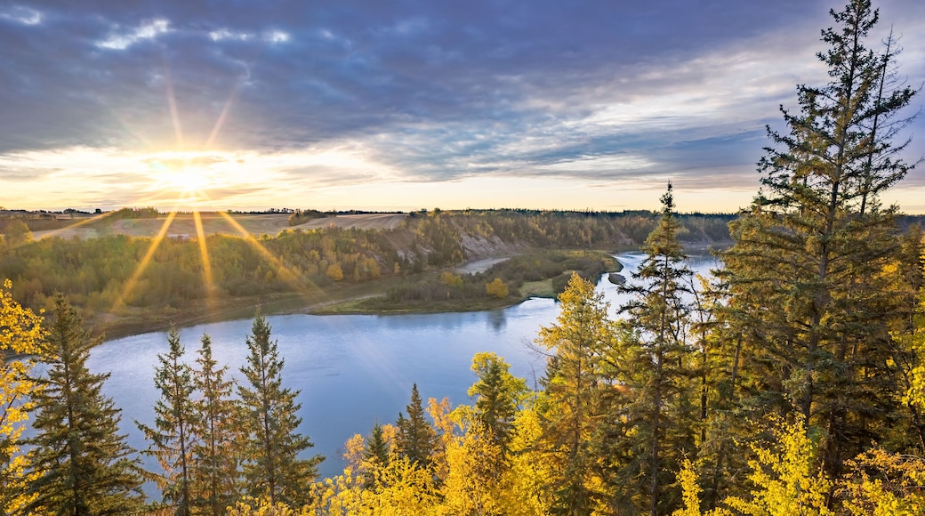 A river winding through a forest with autumn foliage, with the sun setting in the background.