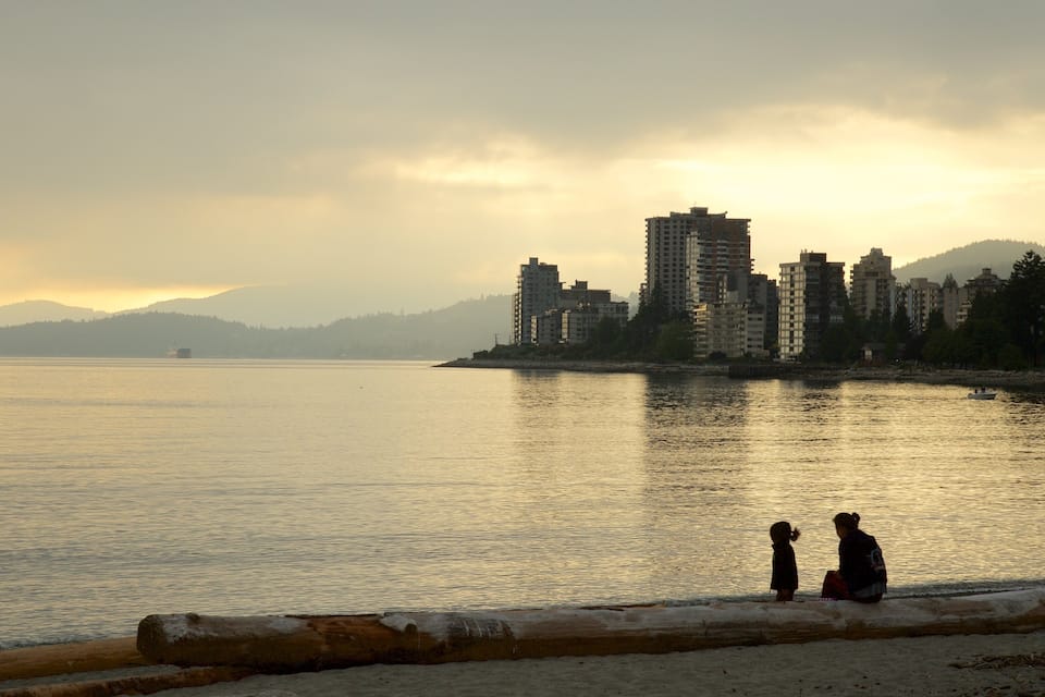 A calm waterfront with buildings and hills in the background.