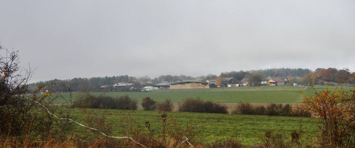 A rural landscape with a large barn, open fields, and scattered houses.