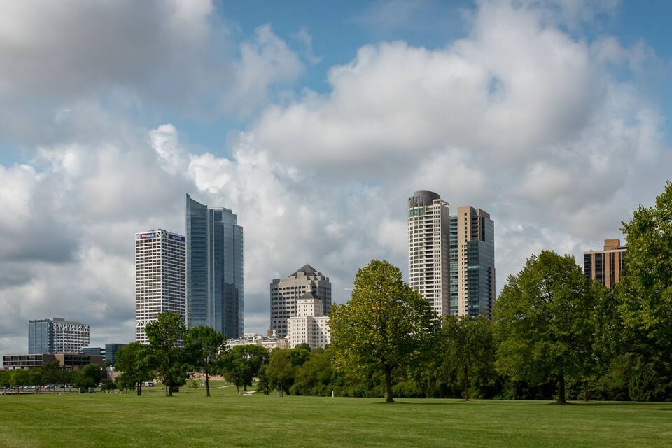 A city skyline with modern skyscrapers and a park with green grass and trees.