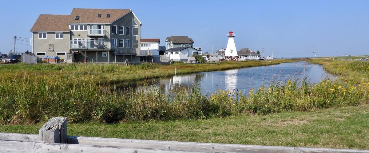 A canal with houses and a lighthouse by the water.