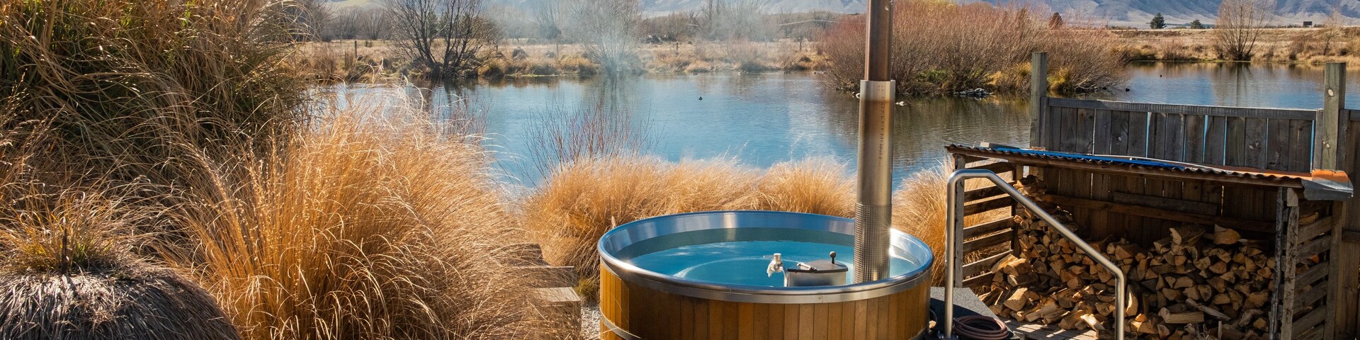 Un jacuzzi junto a un lago, con montañas al fondo.