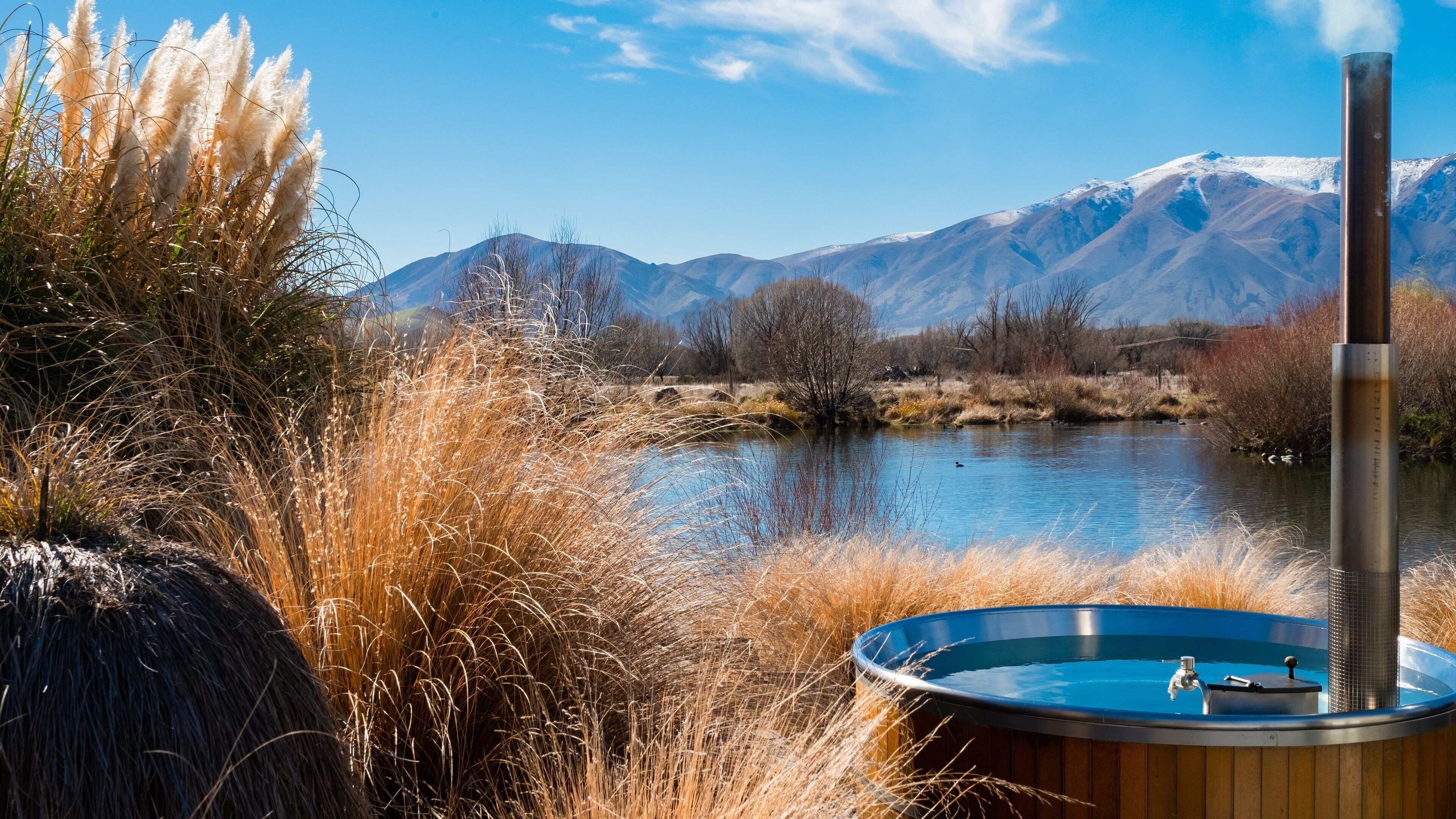 A hot tub by a lake with mountains in the background.