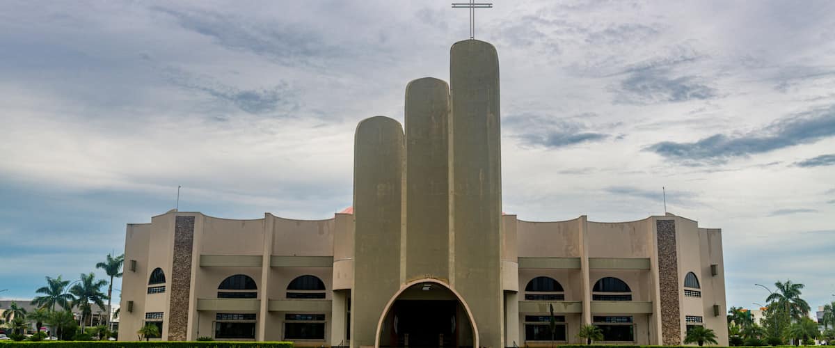 A large building with a central archway, flanked by two vertical structures, and surrounded by a well-maintained lawn.