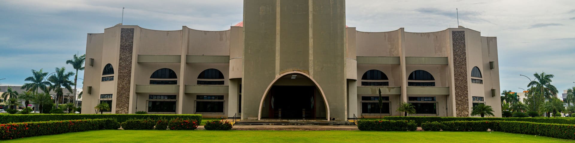 A large building with a central archway, flanked by two vertical structures, and surrounded by a well-maintained lawn.