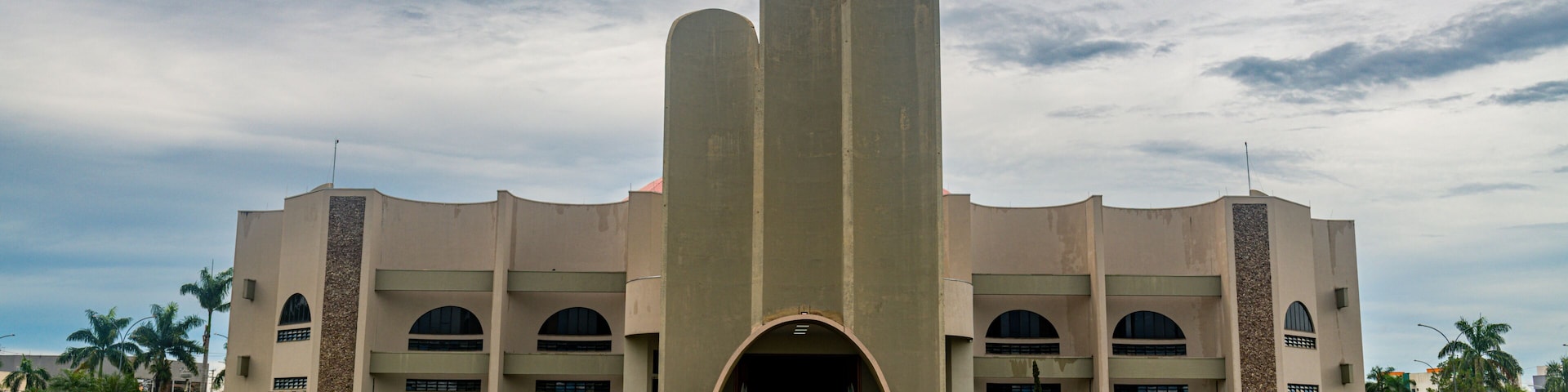 A large building with a central archway, flanked by two vertical structures, and surrounded by a well-maintained lawn.
